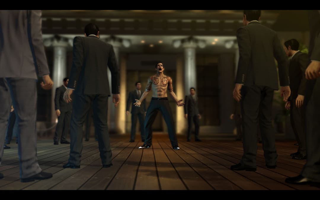 ゲームのスクリーンショットヤクザ0スーツを着た多くの男性の真ん中に6パックの腹筋とタトゥーが叫ぶタトゥーを見せている上半身裸の男を示す