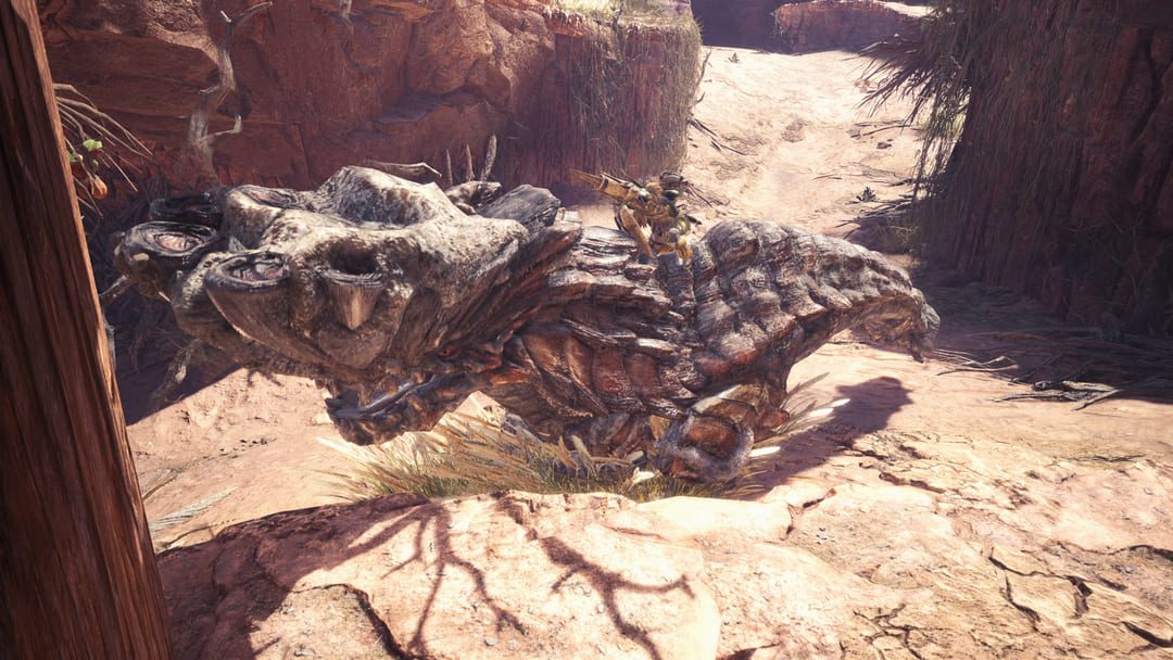 ゲームモンスターハンターからのスクリーンショット：ハンターが巨大なベージュのスカリーモンスターとレスリングすることを示す世界
