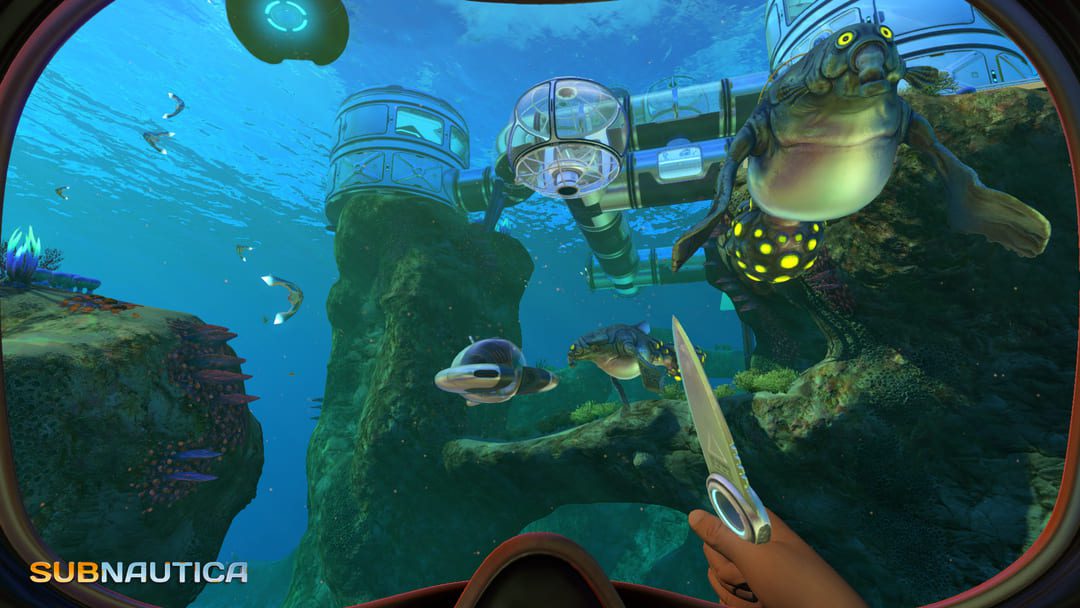 ゲームサブナウティカのスクリーンショットは、エイリアンの魚を見ている水中ダイバーとサンゴ礁の上に建てられた基地の視点を示すスクリーンショット